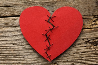 Photo of Broken heart. Torn red paper heart sewed with thread on wooden table, top view