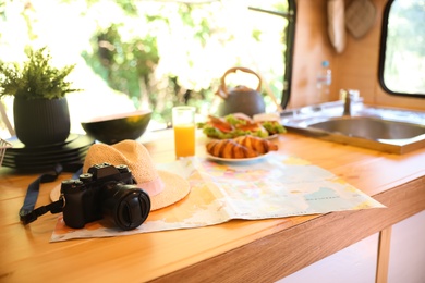 Photo of Camera, hat and world map on wooden table in modern trailer. Camping vacation