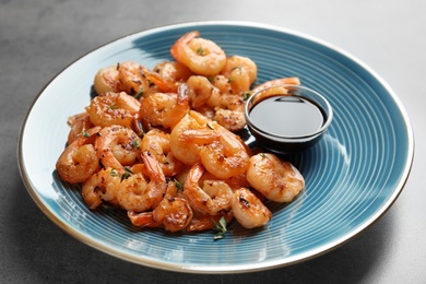 Plate with fried shrimps and soy sauce on grey background