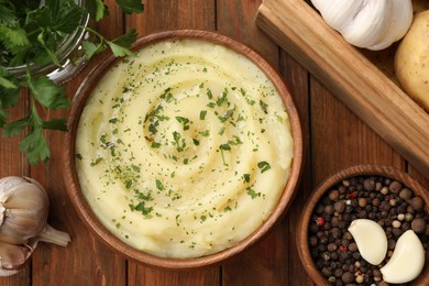 Photo of Bowl of tasty mashed potato, parsley, garlic and pepper on wooden table, flat lay
