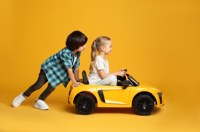 Cute boy pushing children's electric toy car with little girl on yellow background