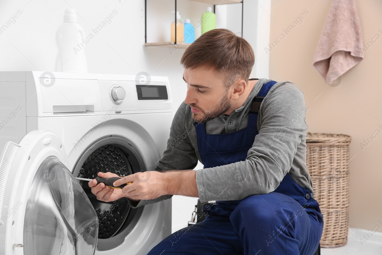 Photo of Young plumber fixing washing machine in bathroom