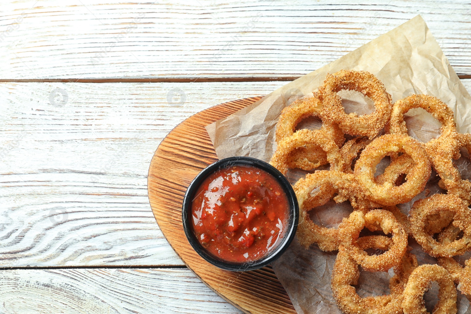 Photo of Homemade crunchy fried onion rings with tomato sauce on wooden table, top view