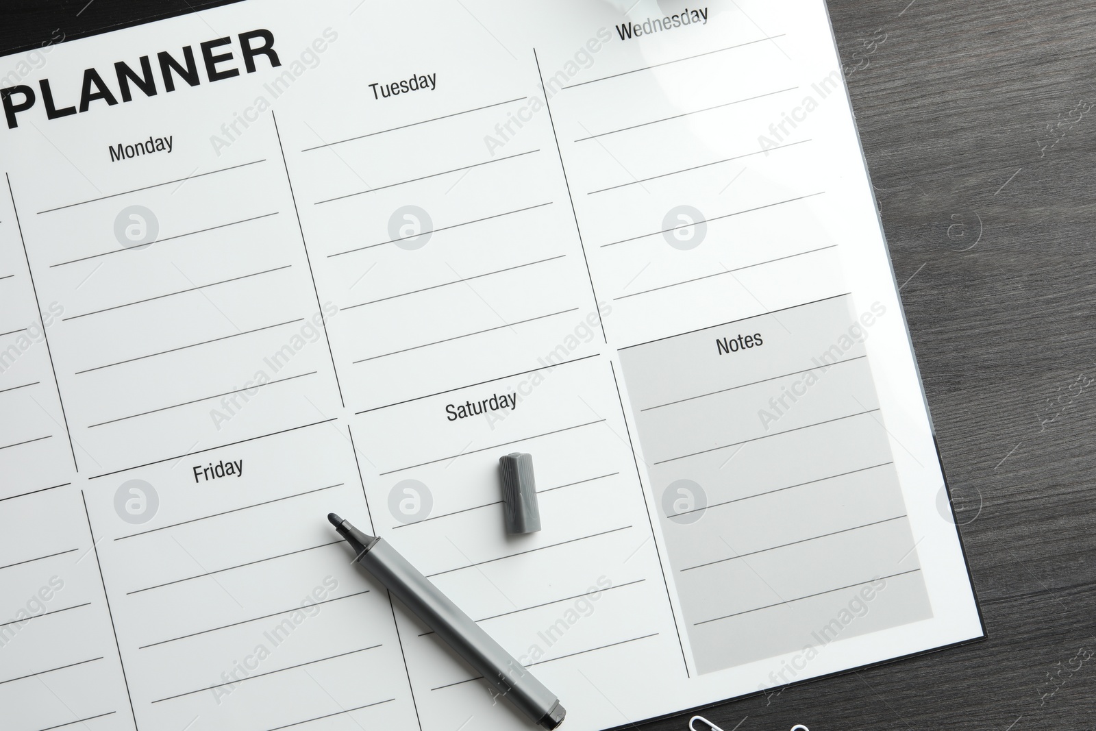 Photo of Timetable. Weekly planner and felt pen on black wooden table, top view