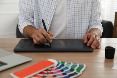 Photo of Professional designer with graphic tablet at wooden table, closeup