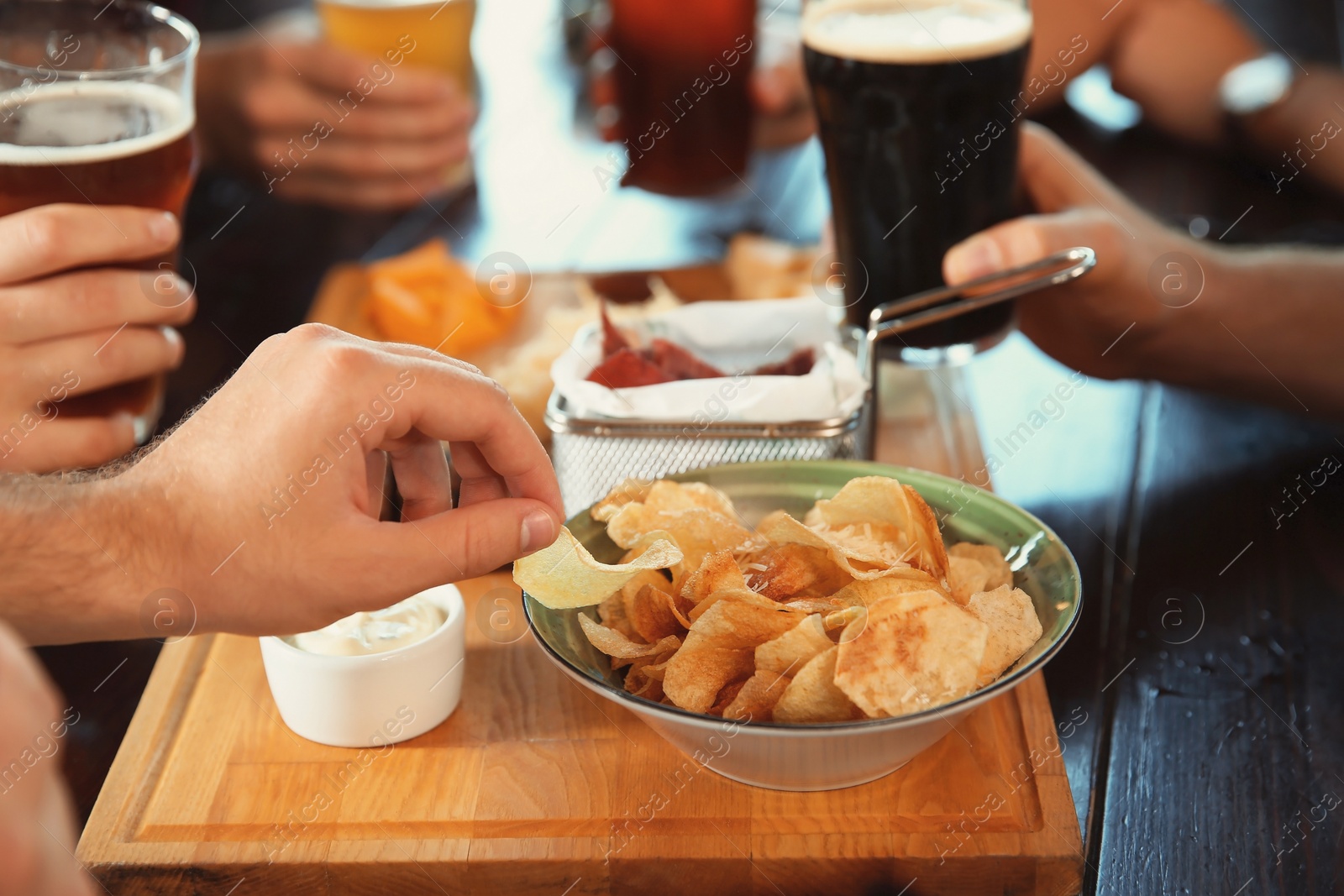 Photo of Friends drinking beer and eating snacks at table in pub