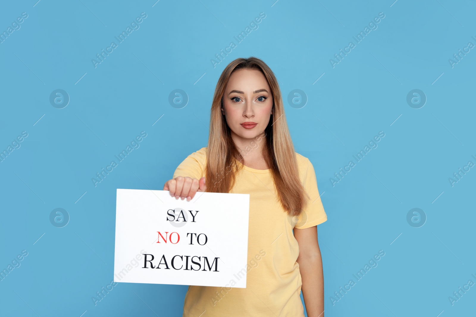 Photo of Young woman holding sign with phrase Say No To Racism on light blue background