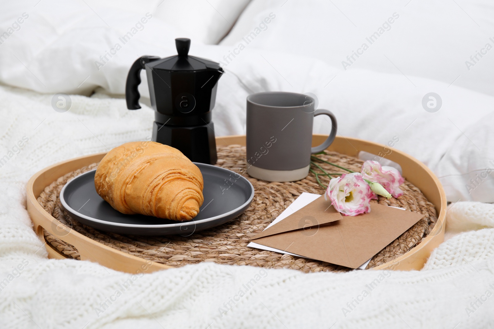 Photo of Tray with tasty croissant, cup of coffee and flowers on white bed