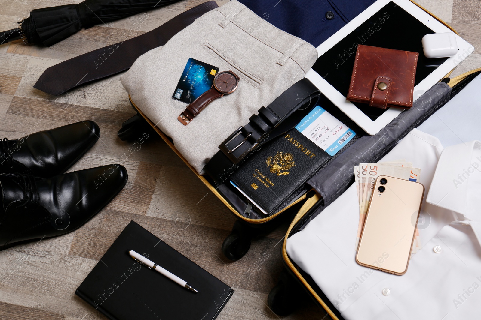 Photo of Packed suitcase with business trip stuff on wooden surface