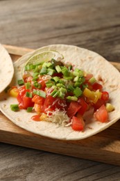 Delicious taco with vegetables, green onion, lime and ketchup on wooden table, closeup