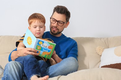 Father reading book with his son on sofa in living room at home