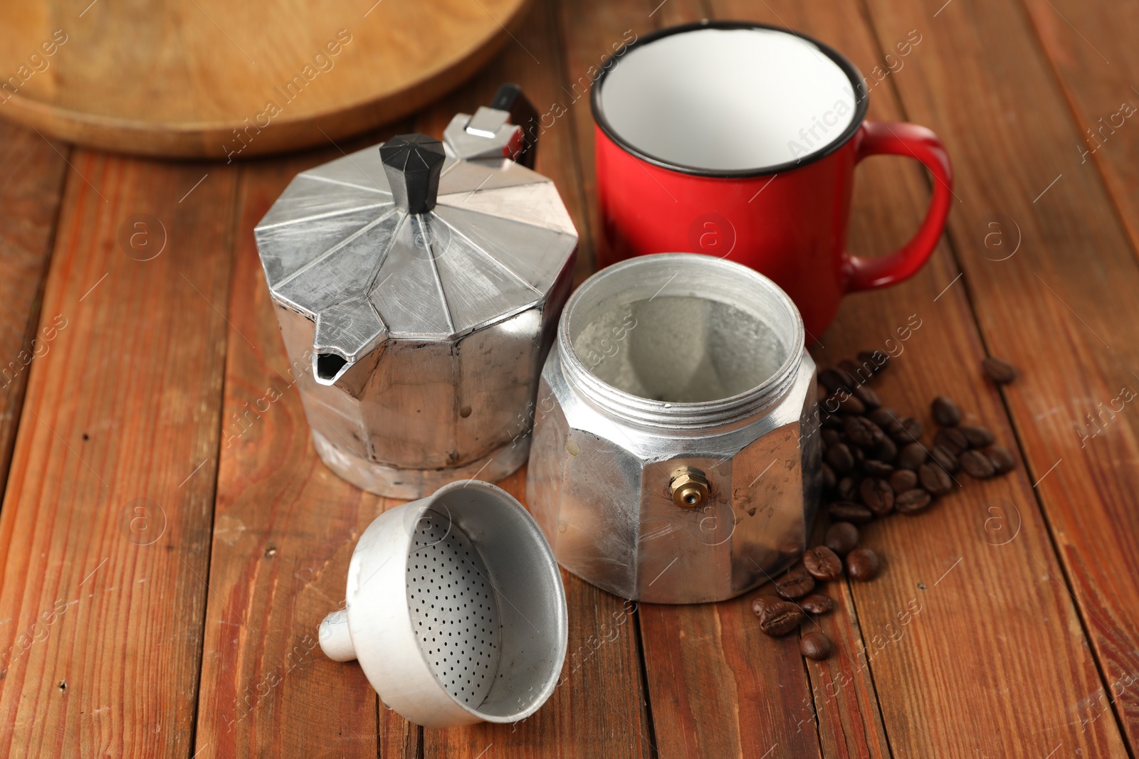 Photo of Moka pot, coffee beans and red mug on wooden table