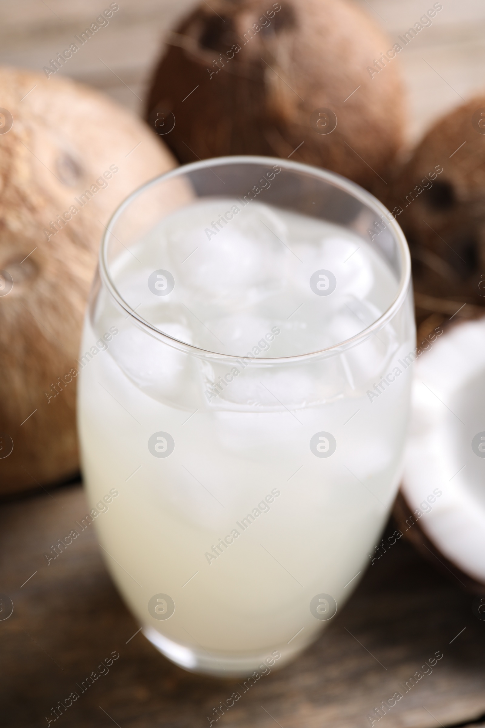 Photo of Glass of coconut water, ice cubes and nuts on wooden table