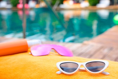 Sunglasses and sunscreen on beach towel near outdoor swimming pool at luxury resort, closeup. Space for text