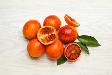 Photo of Many ripe sicilian oranges and leaves on white wooden table, flat lay