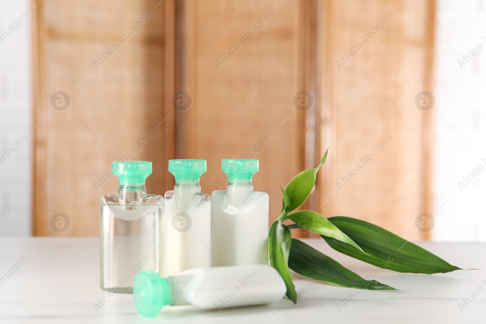 Photo of Mini bottles of cosmetic products and green branch on white table against blurred background