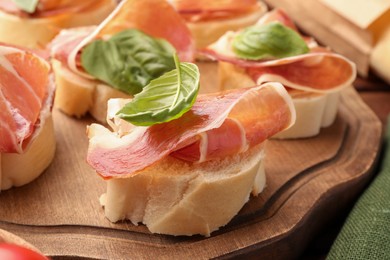 Board of tasty sandwiches with cured ham and basil leaves on table, closeup