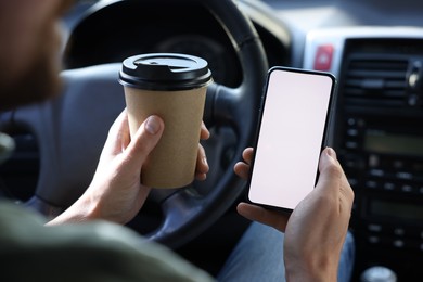 Photo of Coffee to go. Man with paper cup of drink and smartphone in car, closeup