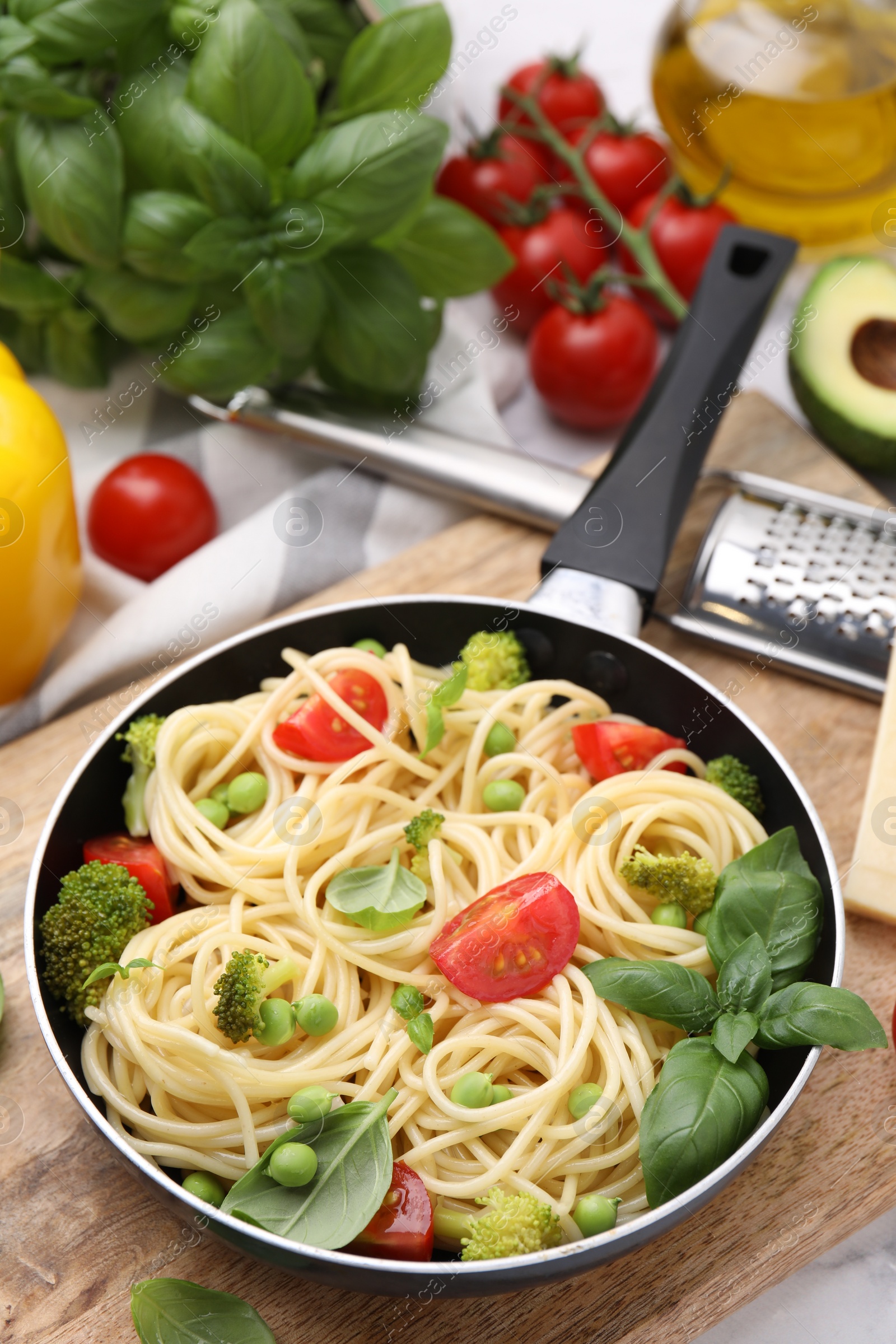 Photo of Delicious pasta primavera in frying pan and ingredients on table, closeup