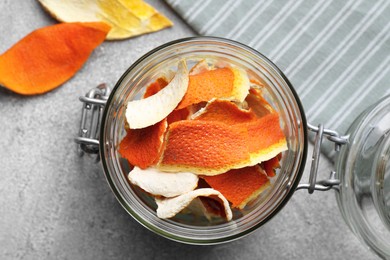 Photo of Glass jar with dry orange peels on light gray textured table, top view