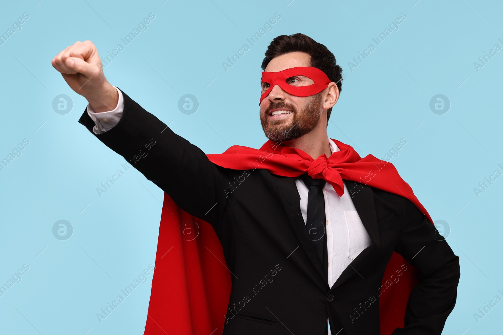 Photo of Businessman wearing red superhero cape and mask on light blue background