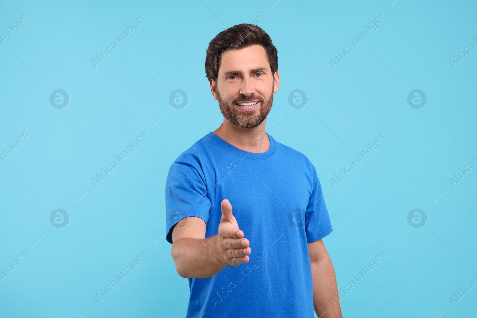 Photo of Happy man welcoming and offering handshake on light blue background