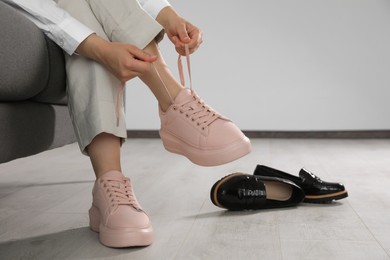 Photo of Woman taking off uncomfortable shoes and putting on sneakers in office, closeup