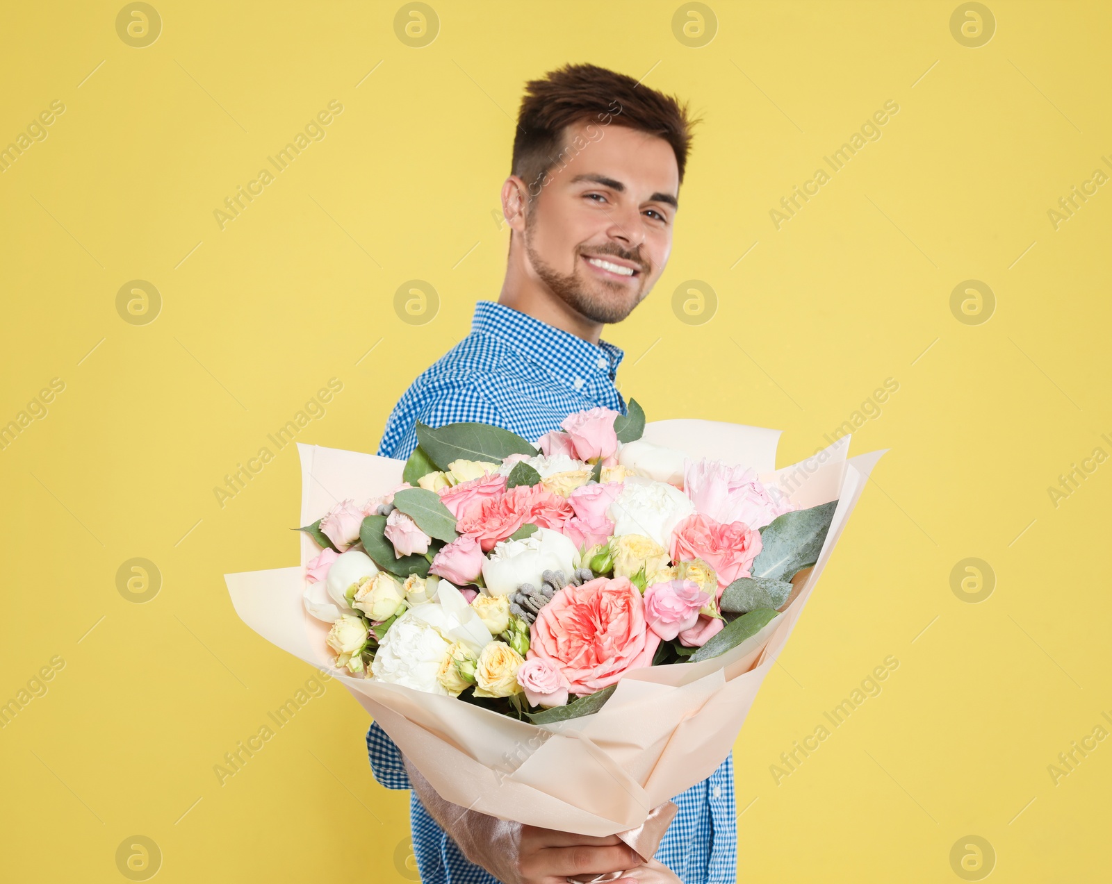 Photo of Young handsome man with beautiful flower bouquet on yellow background