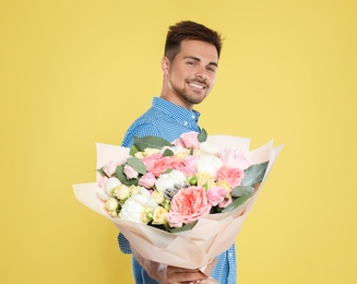 Young handsome man with beautiful flower bouquet on yellow background