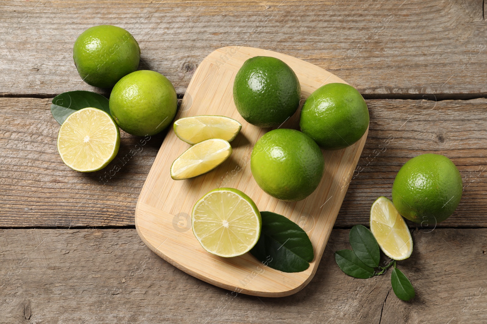 Photo of Fresh limes and green leaves on wooden table, flat lay