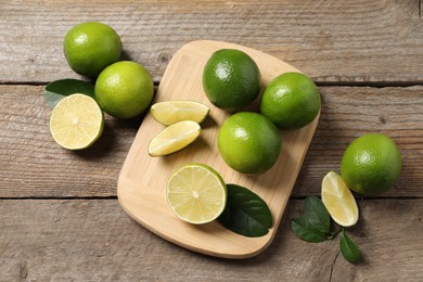 Fresh limes and green leaves on wooden table, flat lay