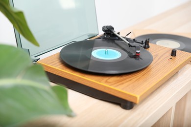 Stylish turntable with vinyl disc on light wooden table indoors