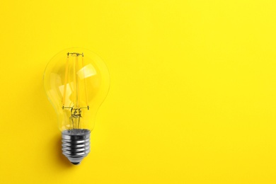 Photo of Vintage filament lamp bulb on yellow background, top view. Space for text