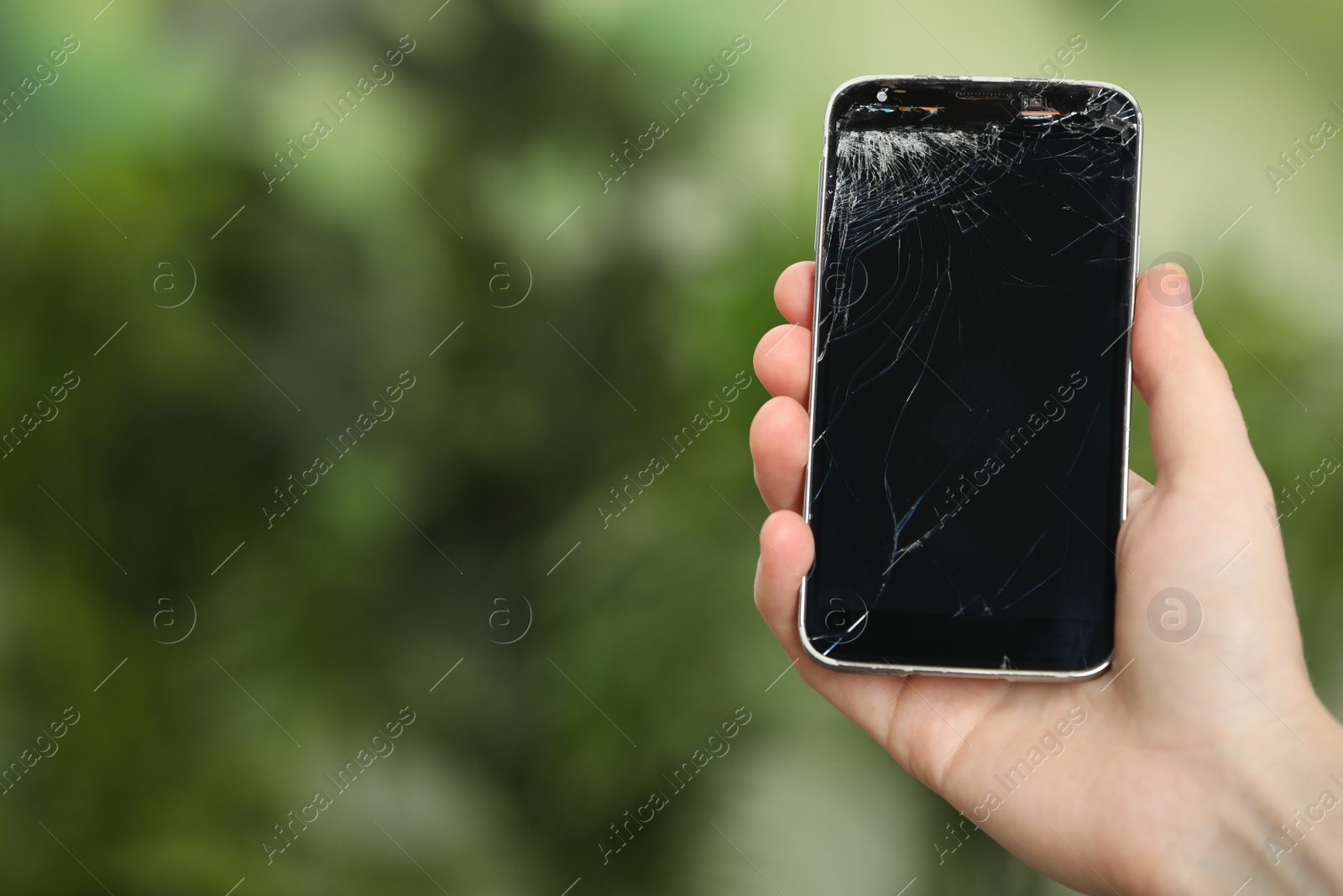 Photo of Woman holding damaged smartphone on blurred green background, closeup with space for text. Device repairing