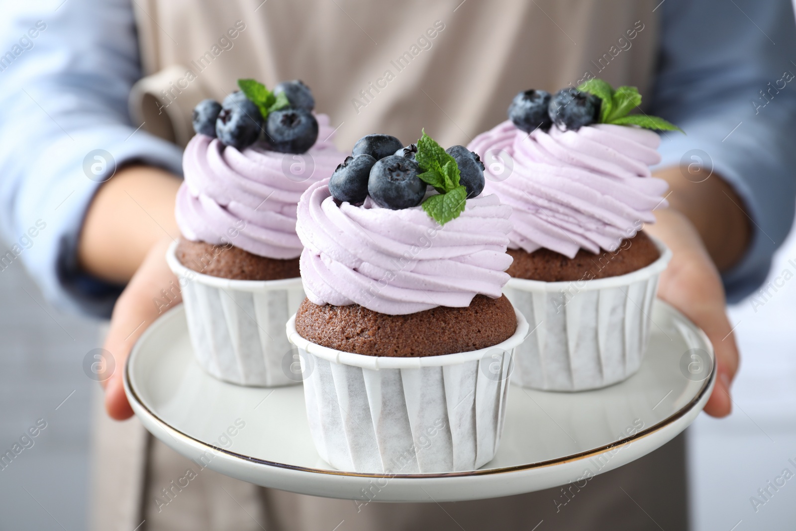 Photo of Woman holding plate with sweet cupcakes, closeup