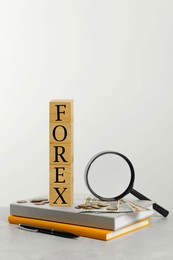 Word Forex made of wooden cubes with letters, magnifying glass and notebooks on light grey table