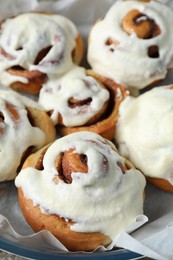 Photo of Many tasty cinnamon rolls with cream in baking dish, closeup