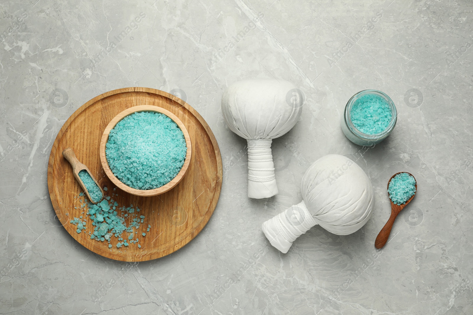 Photo of Spa herbal bags and turquoise sea salt on grey marble table, flat lay