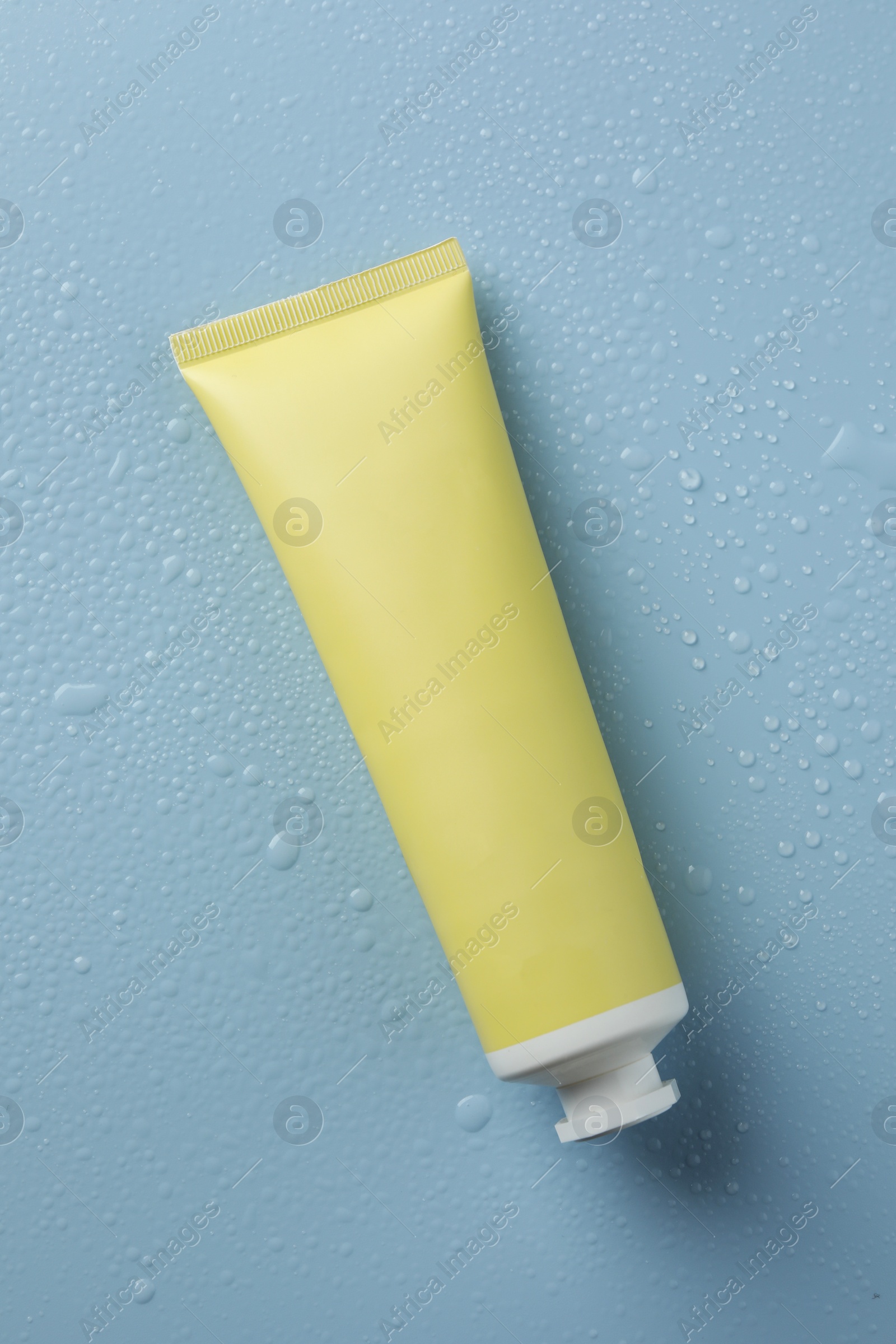 Photo of Moisturizing cream in tube on light blue background with water drops, top view