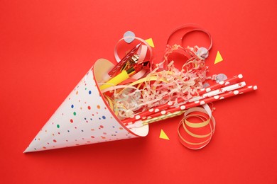 Party hat and different festive items on red background, flat lay
