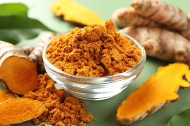 Photo of Aromatic turmeric powder and raw roots on green background, closeup