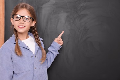 Photo of Smiling schoolgirl in glasses pointing at something on blackboard. Space for text