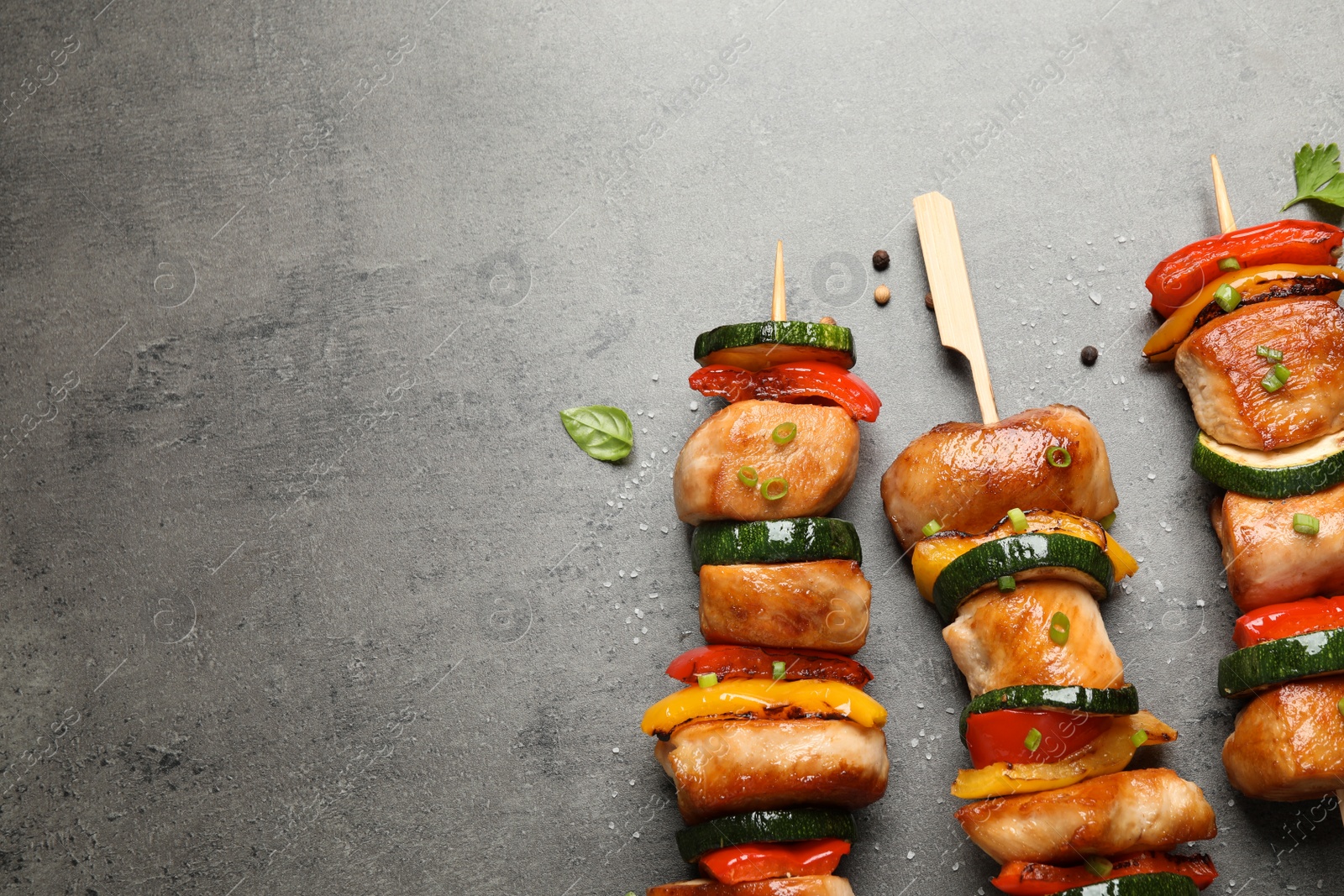 Photo of Delicious chicken shish kebabs with vegetables and herbs on grey table, flat lay. Space for text