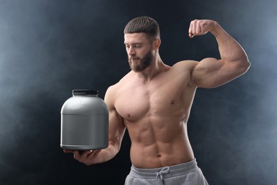 Photo of Young man with muscular body holding jar of protein powder on dark grey background