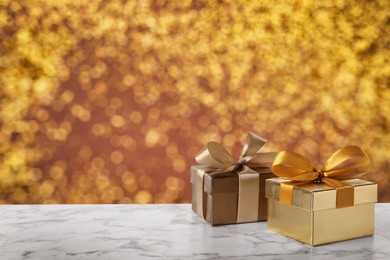 Image of Beautiful gift boxes on white marble table against shiny golden background, bokeh effect. Space for text