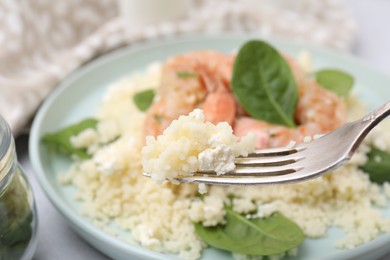 Photo of Fork with delicious couscous over plate, closeup