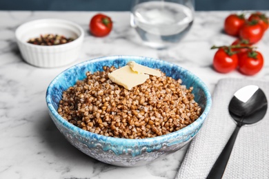 Photo of Bowl of buckwheat porridge with butter served on marble table