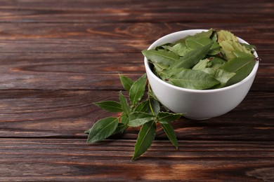 Photo of Fresh green bay leaves in bowl on wooden table, space for text