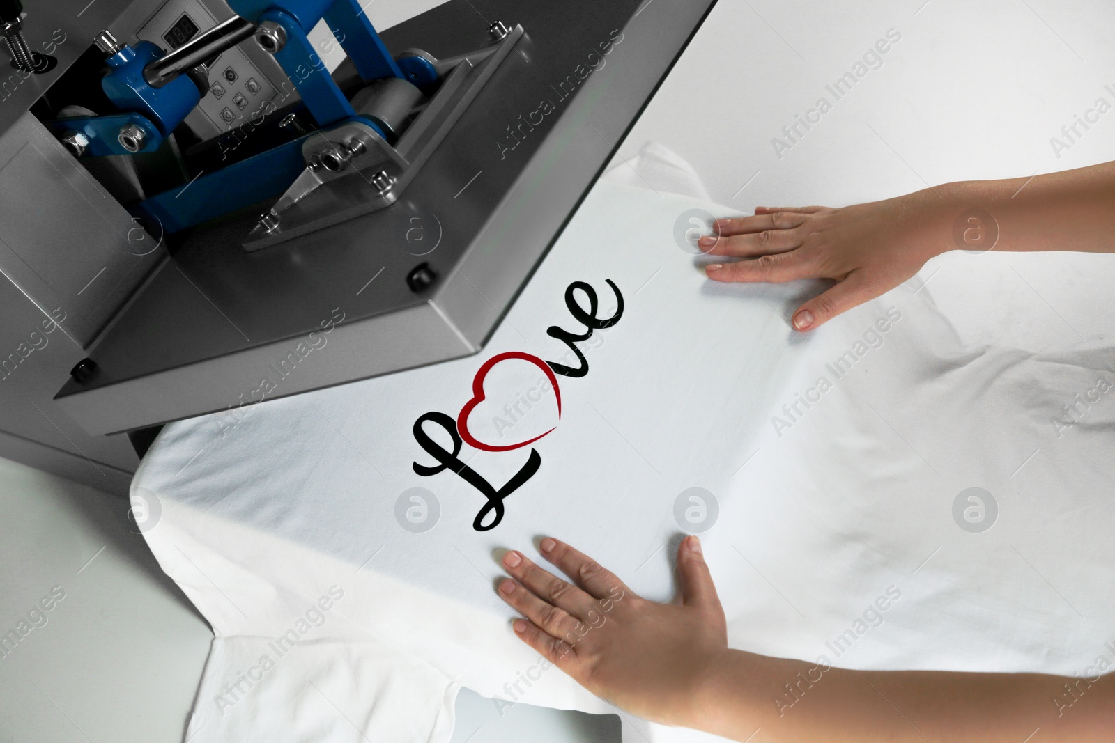 Photo of Printing logo. Woman with t-shirt using heat press at white table, closeup