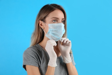 Photo of Woman in medical gloves putting on protective face mask against light blue background